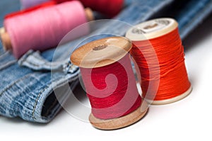 Colorful sewing thread spool bobbins on white table on blue jeans background