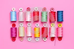 Colorful sewing threads and buttons on pink background. Flat lay, top view, Colorful thread spools and buttons on pink background