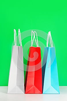 Colorful shopping or gift bags on wooden desk against green background.