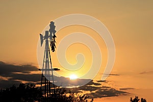 Colorful sky with clouds and a windmill silhouette with orange and yellow sky in Kansas