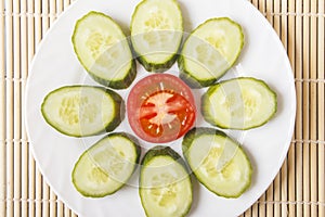 Colorful sliced fresh organic vegetables on white plate. Ripe red tomato and cucumber in form of flower for healthy breakfast or d