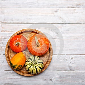 Colorful small pumpkins in round wooden tray on wooden table. Autumn harvest, still life. Fall background. Halloween or