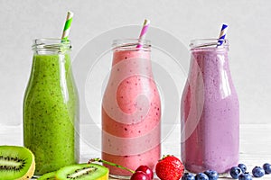 Colorful smoothies in bottles : green, purple and red with fruits and berries