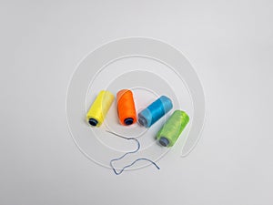 Colorful spools of thread with a needle on a plain white background