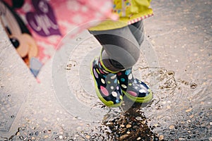 Colorful spotted rain boots baby girl playing with water puddles photo