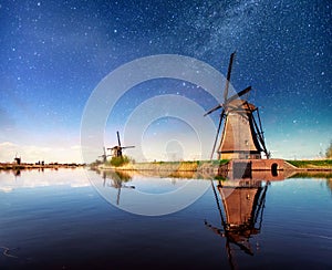 Colorful spring night with traditional Dutch windmills canal in Rotterdam. Wooden pier near the lake shore. Holland