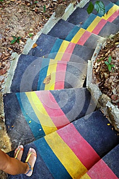 Colorful stairs in jungle and two feet of woman in sandals, top view.