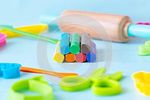 Colorful sticks plasticine with cutters, knife, roller and scissors on a blue background, multicolored modeling clay.