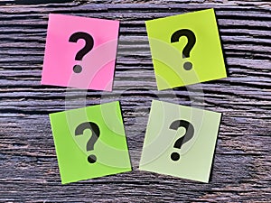 Colorful sticky note written question mark isolated on wooden background.
