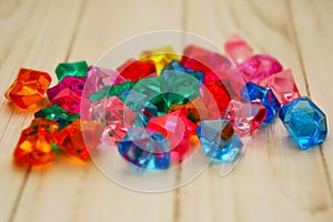 Colorful stones scattered on a wooden table, children`s toys for the development of motor skills of fingers, plastic gems.