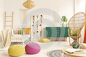 Colorful and stylish boho kid`s bedroom with peacock chair, single metal bed and green wooden cabinet