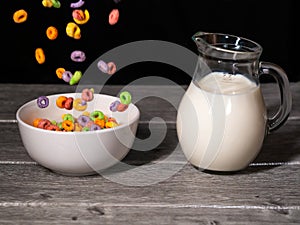 Colorful sugary cereals falling into a white bowl and milk jug in the background