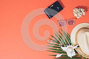 Colorful summer holidays fashion flat lay - straw hat, camera, sunglasses, sea shells on bright orange background