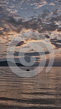 Colorful summer sunset on bay. Scenic dramatic clouds on sky. Boat with two people