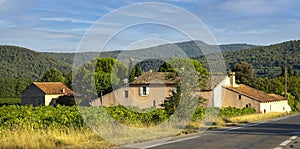 Colorful sunny summer landscape with mountains, forest, trees, houses, road. The house stands next to the road among the trees.