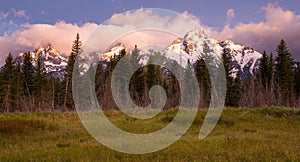 Colorful sunrise and clouds over snowy mountains above a grassy meadow