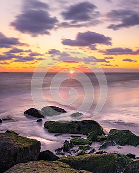 Colorful sunset glow and dramatic clouds over jetty rocks in the ocean