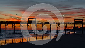Colorful Sunset at ocean coast with silhouette of pier and photo