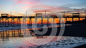 Colorful Sunset at ocean coast with silhouette of pier and photo