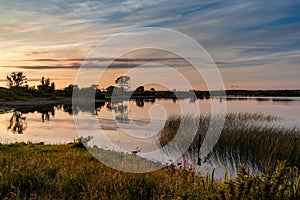 Colorful sunset over a calm lake with reflections and reeds in the foreground