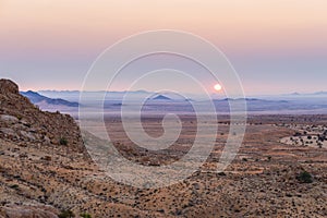 Colorful sunset over the Namib desert, Aus, Namibia, Africa. Orange red violet clear sky at the horizon, glowing rocks and canyon