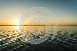 Colorful sunset over water surface, evening sun over the bay, summer sky without clouds