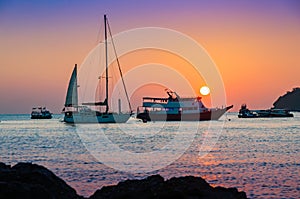 Colorful sunset with sailboat passenger boat and motor boats doc