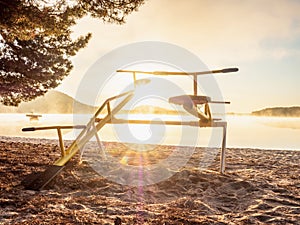 Colorful sunset with seesaw on beach. Teeter totter with wooden chairs