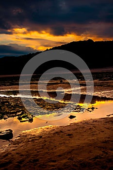 a colorful sunset on the shore of a beach, with small rocky shoreline
