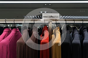 Colorful sweaters hanging in clothing retail store. New collection nameplate.