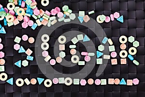 Colorful sweet candy with a word sugar on black background.
