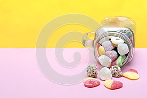 Colorful sweet different jelly candies in glass jar cup lying isolated on pink yellow background, pastry, confectionery, desserts