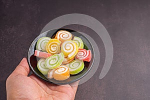 Colorful sweet jelly candy on a black plate on a palm with a dark brown background. Jelly circle breaded in sugar. Top view
