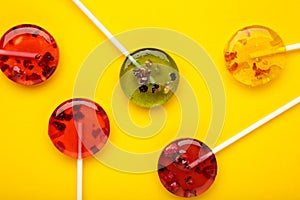 Colorful sweet lollipops with berries on yellow background