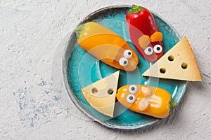 Colourful sweet mini peppers in the shape of mouses and pieces of cheese on a plate, stone table, top view, snack for kids idea