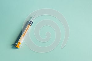 A colorful  syringe with the needle uncapped on textured bluish paper background.