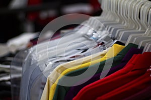 Colorful t-shirts on hang for sale in shop. Multicolored summer polo on hanger.