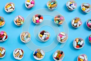 Colorful tablets with capsules and pills in cupcake wrappers on blue background