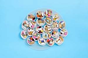 Colorful tablets with capsules and pills in cupcake wrappers on blue background