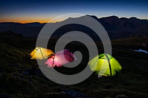 Colorful tents lit up in a lake district at national park with Scafell Pike at nightfall