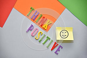 Colorful THINK POSITIVE text on the red, orange and green background. Smile icon on the sticky note. Lifestyle concept