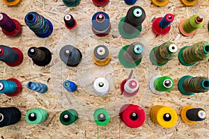 Colorful thread reels on wooden wall set up for sewing machine, textile industry factory