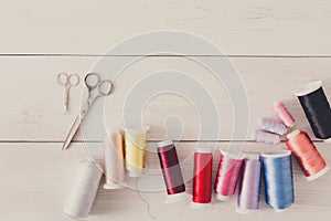 Colorful thread spools and scissors on wooden table flat lay