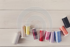 Colorful thread spools on wooden table flat lay