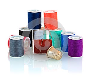 Colorful threads, thimble and needle isolated on white background with shadow reflection. Tools for sewing on white backdrop.