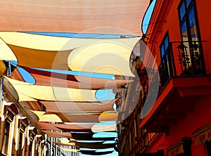 colorful tightly weaved sun sail UV protection fabric suspended from exterior walls over the street