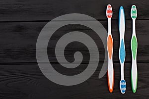 Colorful toothbrushes on black wooden background.