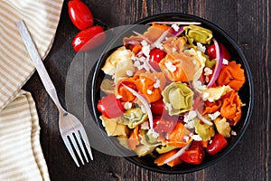 Colorful tortellini pasta salad, overhead scene on dark wood