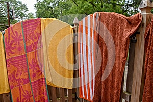 Colorful towels spread opened and hanging on a wooden fence near a backyard swimming pool on a sunny summer day