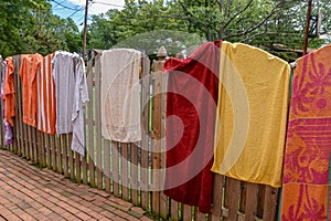 Colorful towels spread opened and hanging on a wooden fence near a backyard swimming pool on a sunny summer day